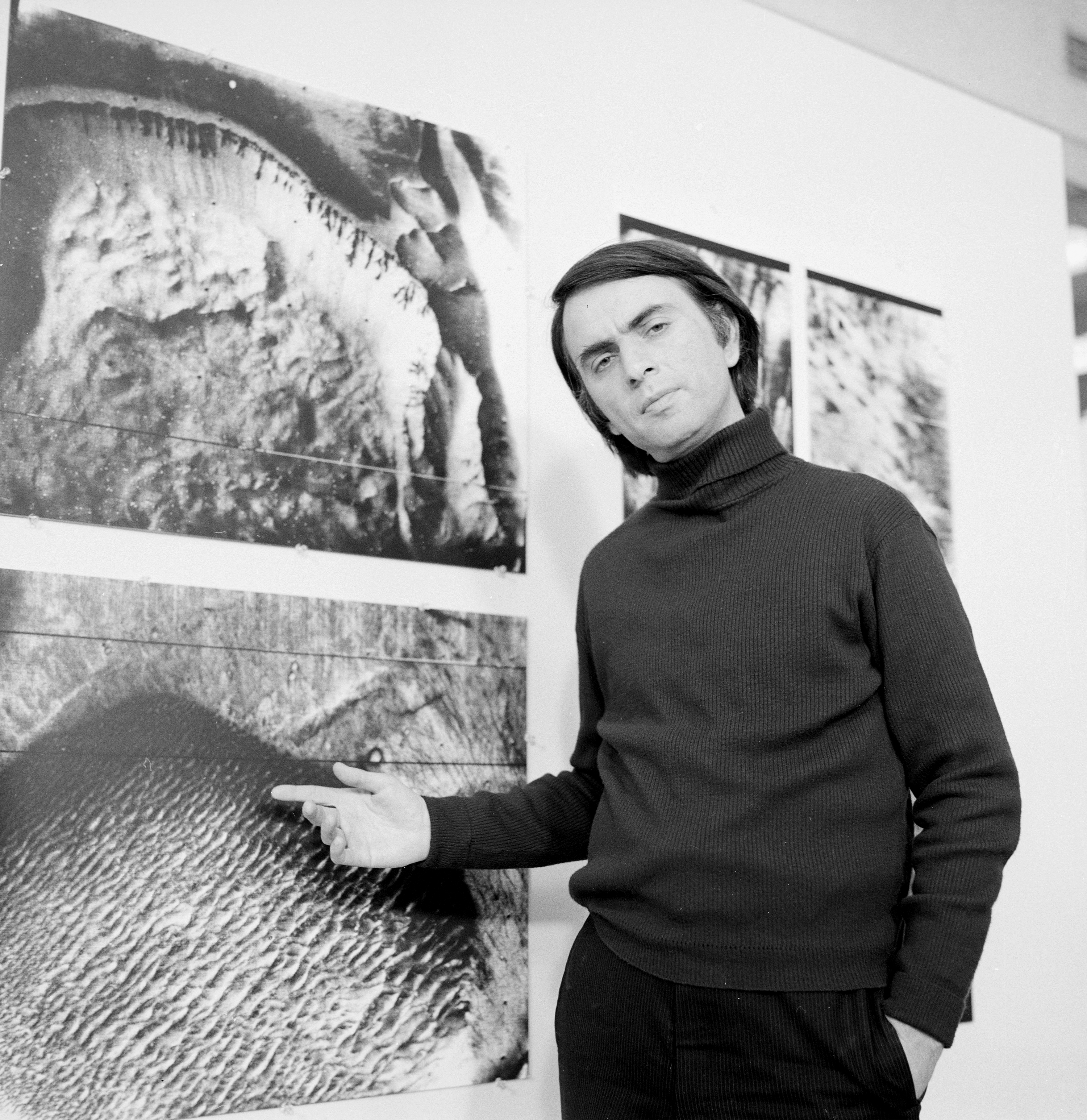 Carl Sagan standing beside planetary maps in a NASA/JPL archival photograph.